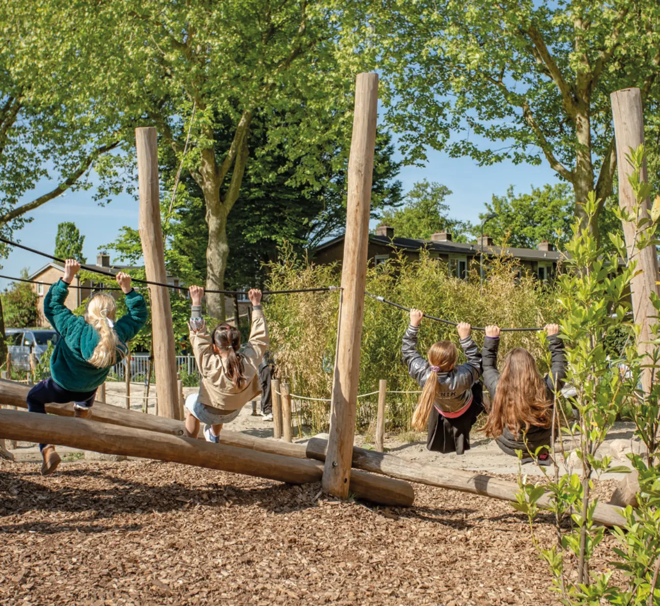 Kinderen klimmen en slingeren aan touwen tussen houten palen op een groen schoolplein